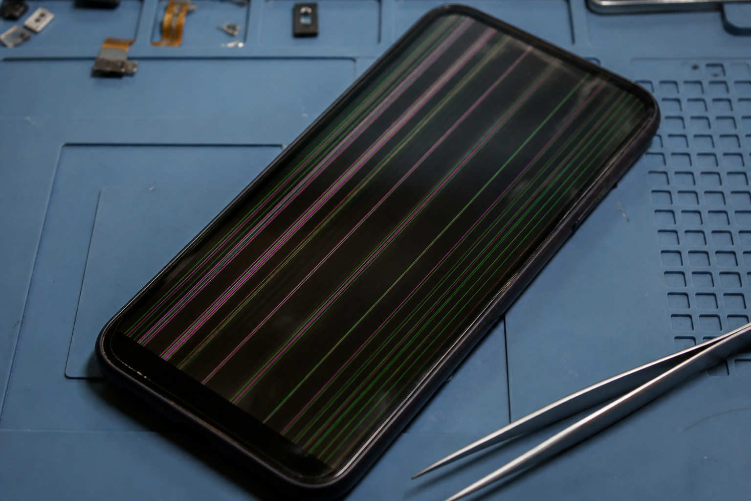 Pantalla de iPhone con líneas verticales de colores sobre esterilla de reparación