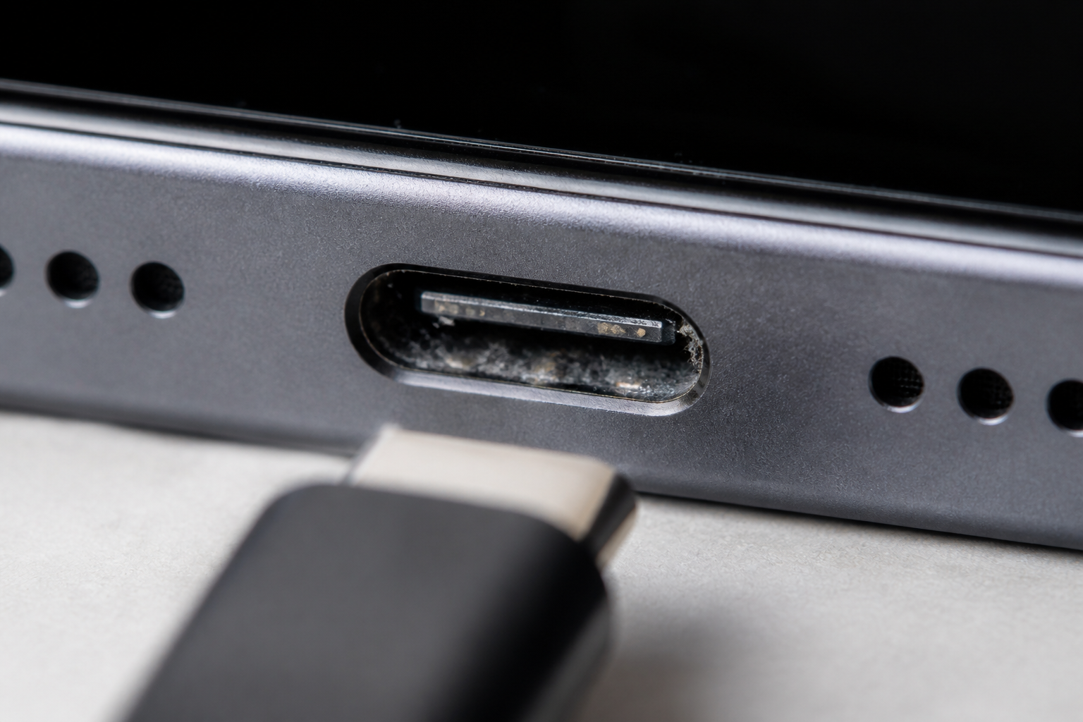 Detalle del puerto USB-C de un iPhone con suciedad y cable de carga
